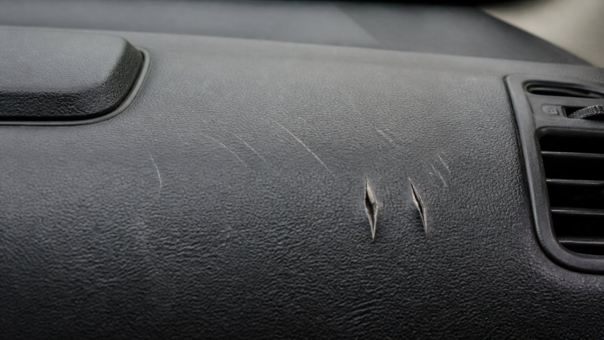 Close-up of car dashboard showing various scratch depths, light surface scratches and deeper gouges, with natural lighting to highlight the damage clearly