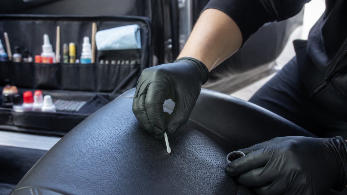 Technician using an applicator to perform car interior repair on a cigarette burn in a black leather seat